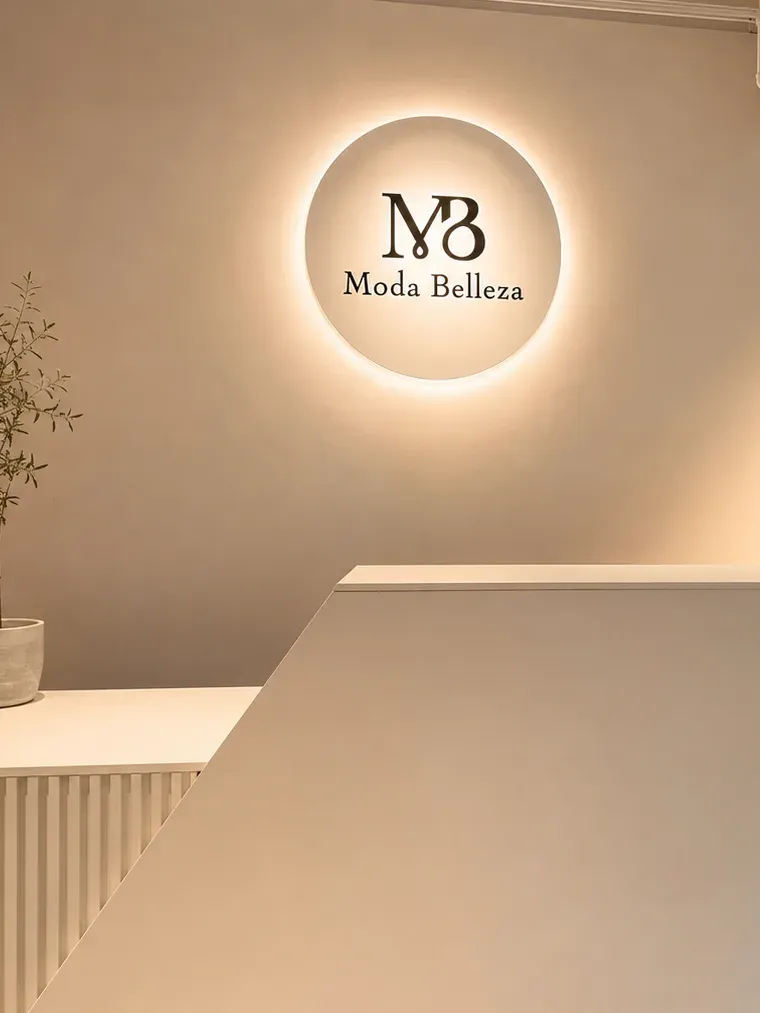 Beleuchtetes rundes Signet von Moda Belleza an der Wand hinter dem Verkaufstresen.